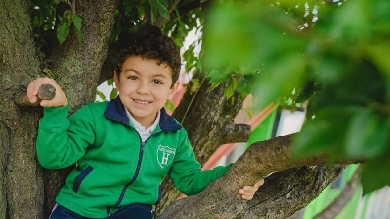 Alumno del Instituto Highlanders con el uniforme verde, trepado en un árbol del patio