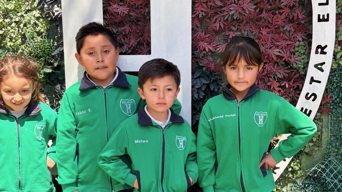 Grupo de alumnos frente al muro verde del colegio con la H y el lema del escudo