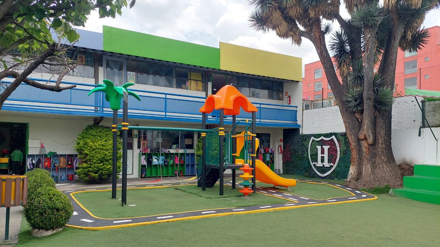 Patio del Instituto Highlanders con pasto sintético, juegos infantiles nuevos y el escudo del colegio en el muro verde